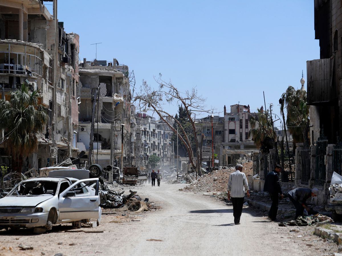 Syrians walk past the ruins of Douma in April 2018