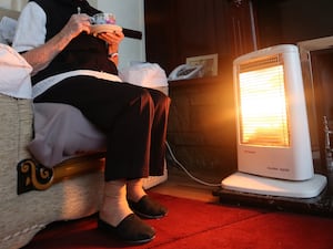 An elderly person sits next to an electric heater