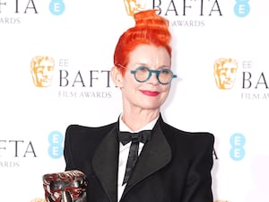 Sandy Powell smiles with Bafta award on red carpet