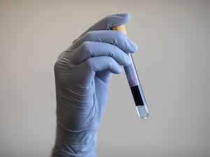 Person in blue gloves holding a test tube that contains blood