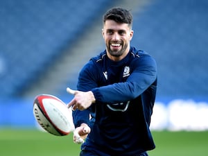 Adam Hastings smiles as he passes a rugby ball