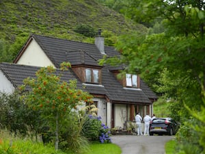 Police outside a house, which is surrounded by trees and shrubs