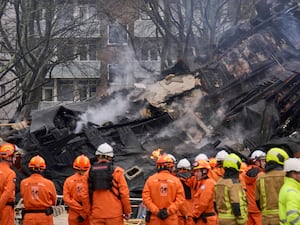 Firefighters standing in front of a demolished apartment block