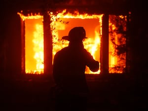 A firefighter is silhouetted in front of a burning structure