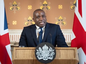 David Lammy giving a speech from behind a lectern with the UK Government crest and flanked by Union flags