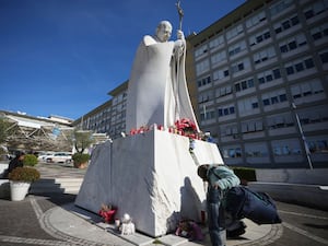 Woman kneeling at statue of Pope John Paul 11 outside a hospital