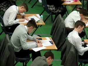 Schoolboys sit in an exam hall writing in exam booklets