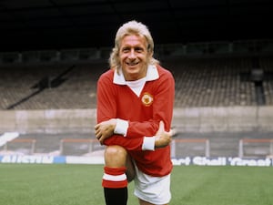 Denis Law smiles while wearing Manchester United kit