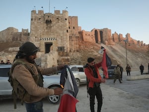 Two fighters burning the Syrian flag outside a castle