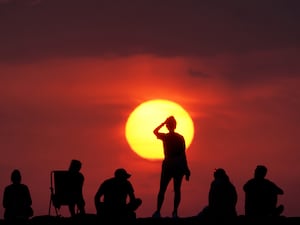 People sit and stand silhouetted in front of the sun