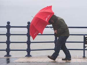 A man battles strong winds with a red umbrella