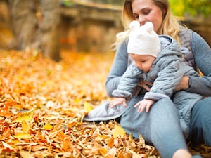 A child being held by their mother in a pile of leaves