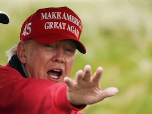 Donald Trump, with his hand outstretched towards the camera, wearing a red baseball cap with the slogan "Make America Great Again"