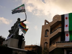 People wave Syrian flags, a huge flag hangs off a building in the background