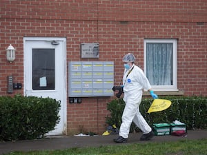 Forensic officer in white protective suit outside a property