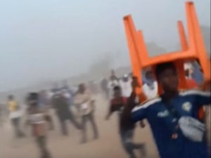 A man holds a chair on top of his head in a stampede,