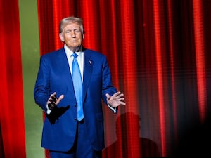 Donald Trump, hands spread, appears before a red curtain on stage