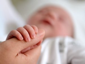 A new born baby grasps the thumb of her mother