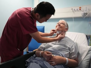 Woman has neck and jaw checked by a doctor in burgundy scrubs