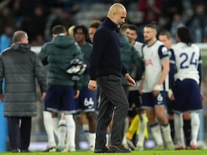 Pep Guardiola appears dejected as he leaves the pitch while Tottenham celebrate in the background