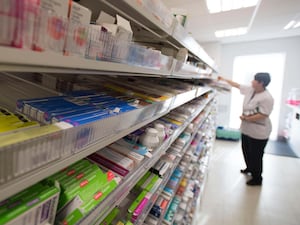 A pharmacist takes something from a shelf, with medications in the foreground