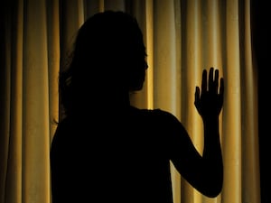 Silhouette of a young woman in front of closed blinds