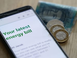 An online energy bill on a smartphone next to some coins and a five pound note