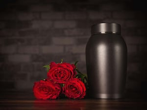 A cremation urn next to three red roses