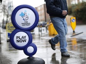 A man walking past a National Lottery sign