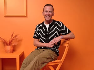 Radio DJ Scott Mills sitting on an orange chair in front of an orange wall