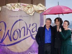 Hugh Grant, Timothee Chalamet and Olivia Colman shelter beneath an umbrella during a photo call with the cast of Wonka