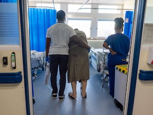 An elderly patient being assisted by NHS staff on a hospital ward