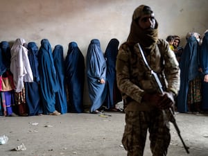 A Taliban fighter stands guard as women wait to receive food rations distributed by a humanitarian aid group in Kabul, Afghanistan