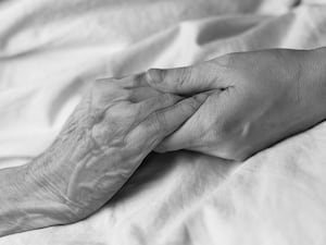 A young woman holding the hand of an old woman in a hospital bed