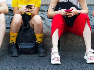 A group of teenagers sitting with phones on a pavement