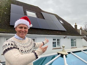 Max Wilkinson, wearing a Santa hat and pointing to solar panels on a roof, has called for new builds to come with solar panels as standard amid efforts to reduce carbon emissions and cut bills