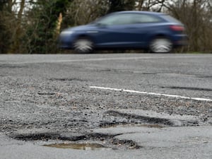 A car drives along a road with potholes