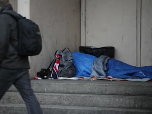 A person walks past a homeless person in a sleeping bag in a doorway