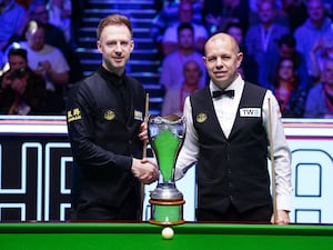 Judd Trump shakes hands with Barry Hawkins in front of the UK Championship trophy