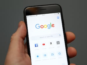 Hand holding a mobile phone showing Google search engine