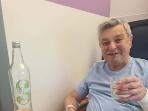 Man dressed in a blue t-shirt in hospital holding a glass