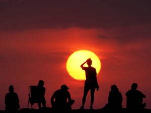 People sitting and standing in front of the sunrise