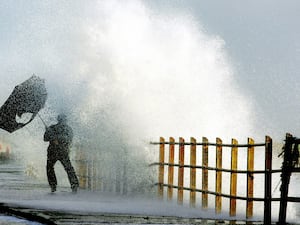 Man with inside umbrella as high waves lap over a harbour wall