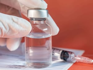 Vial of vaccine with a medical gloved hand on it, next to a syringe