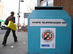 A person walks past a blue Knife Surrender Bin for depositing knives, with a Metropolitan Police sticker on the side reading 'Get A Life, Bin That Knife', in Kings Road, London