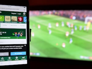 Gambling site on a smartphone in front of football being shown on a TV