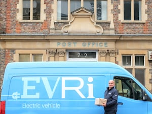 A person stands beside an Evri van holding a parcel