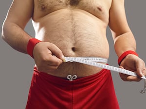 An overweight man measuring his waist with a tape measure