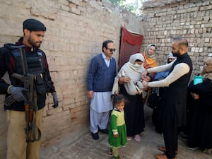 A police officer stands guard as a health worker administers a polio vaccine to a child, in Peshawar, Pakistan