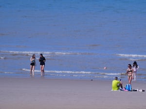 Beachgoers sit and walk by the waters of a beach